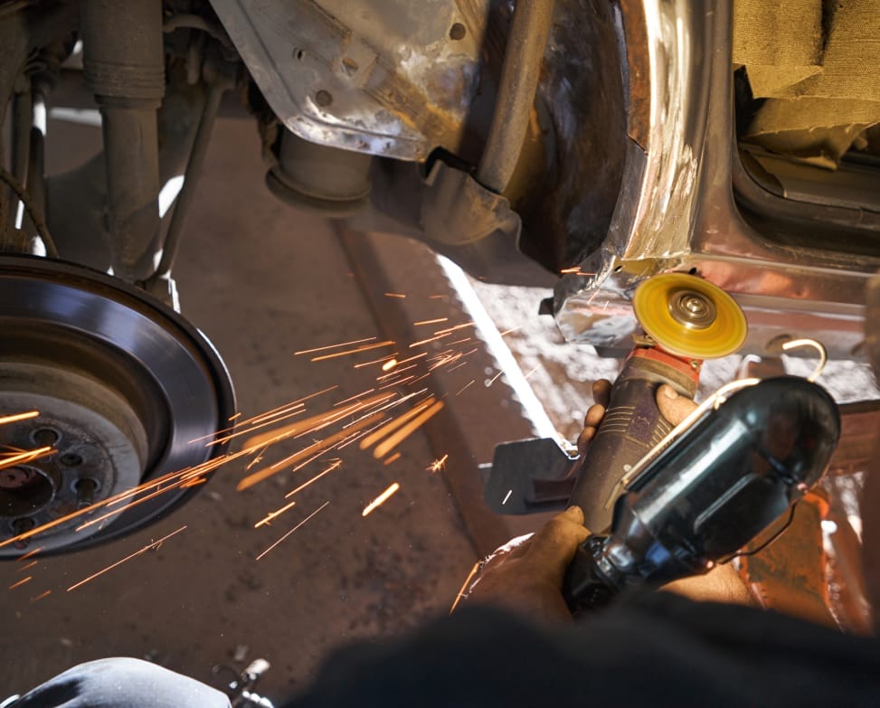 Close-up photo of man working with angle grinder, cleaning welding seams with grinder on car in garage